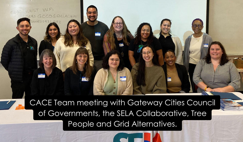 Fourteen people smiling, sitting and standing behind a table. People shown are CACE staff, partners from Gateway Cities Council of Governments, the SELA Collaborative, Tree People and Grid Alternatives.