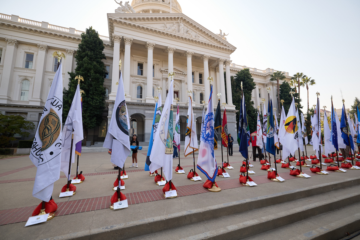 Flags representing Native American Tribes within California line the west steps of the Capitol Building.