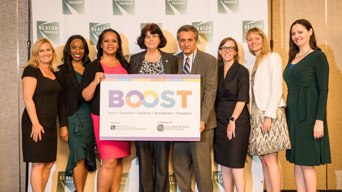 SGC, ILG and City of Palo Alto leadership and staff pose with a sign that says 'BOOST'.
