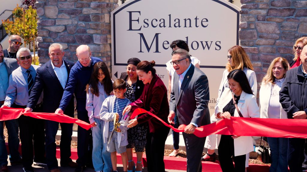 Multiple people cutting red ribbon in front of Escalante Meadows sign.