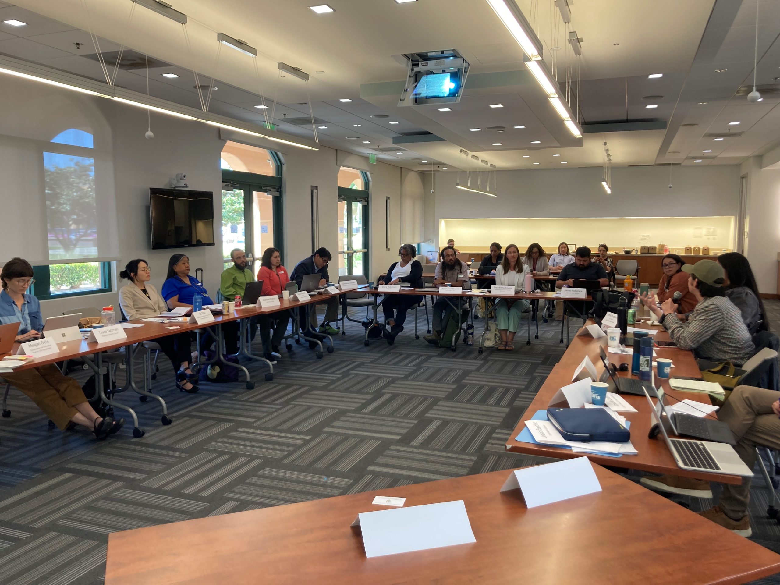 The members of the California Agricultural Land Equity Task Force sit around a U-shaped arrangement of tables at a Task Force meeting in San Diego, CA. Task Force member Dorian Payán is speaking to the group holding a microphone.